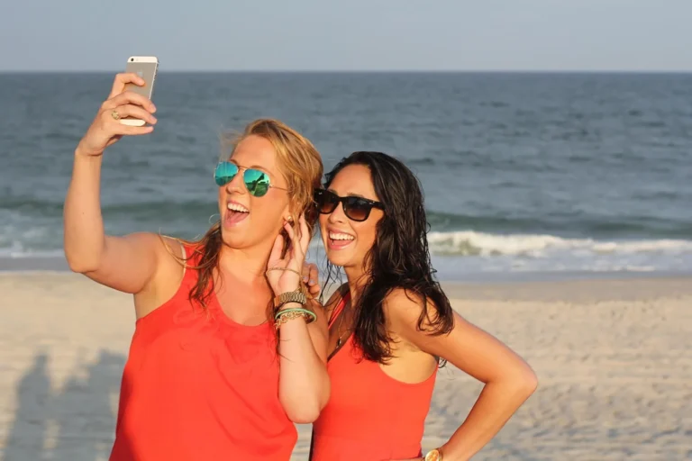 Dwie roześmiane przyjaciółki robią sobie selfie na plaży